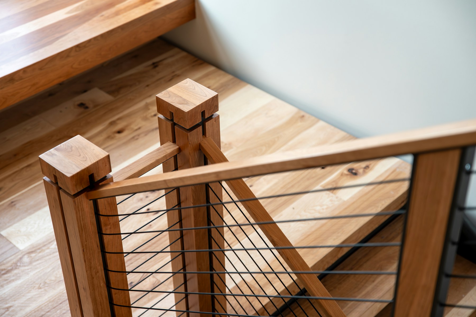 Thin horizontal black cables tensioned between cherry-wood stair posts